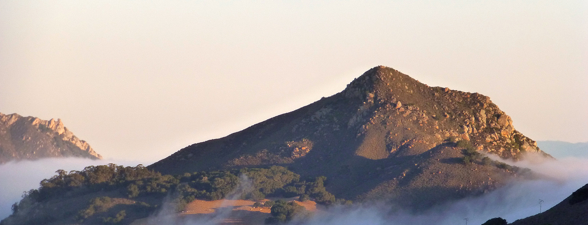 Cerro Ramauldo, one of the nine rocky peaks in San Luis Obispo County. Depicts a mountain with oak trees and large granite blocks. Click to view article, County of San Luis Obispo Closed the Oklahoma Parking Site