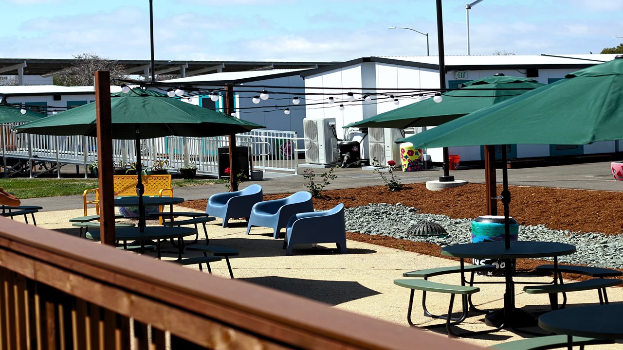 Inside the Hope Village supportive housing community. Pictured are community tables shaded by green umbrellas.