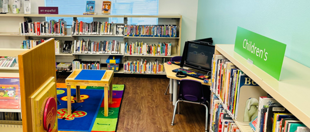 Image of the Children's section of the library, including a table on a colorful rug and computers