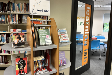 Image of books on display on shelves in the library. The shelf has a sign that reads 