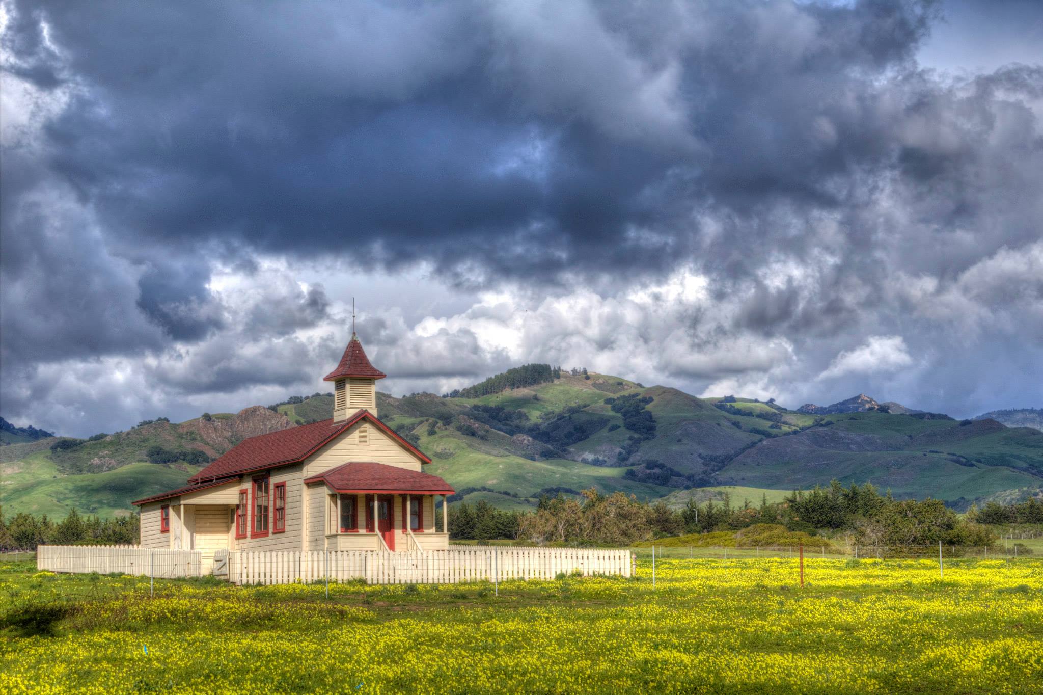 Cloudy day in San Simeon, an old schoolhouse surrounded by a picket fence in an open field