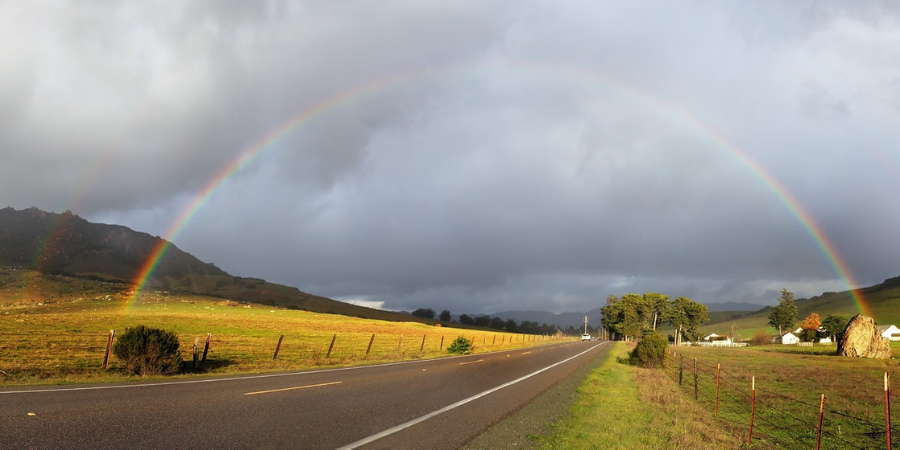 Rainbow over road between green hills