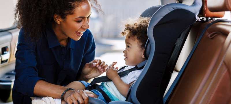 Woman and child happily ensuring that the child's car seat is securely fastened.