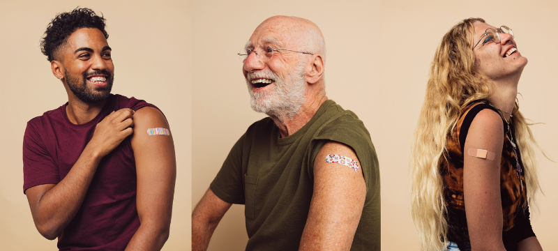 A young man, and older man, and a young woman smiling, showing off their bandaids on their shoulders.