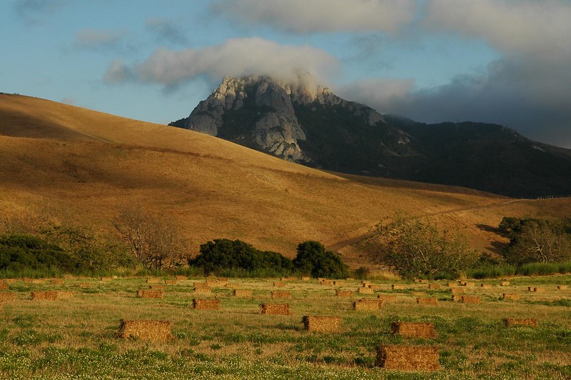 Holister Peak surrounded by clouds. In the foreground are brown hills and hay bales. 