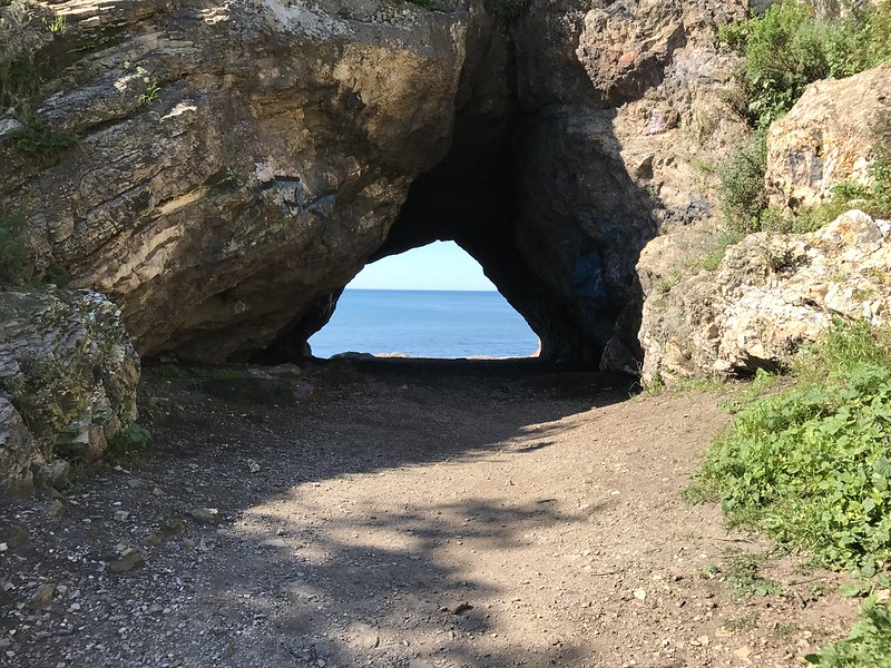Dirt path leading up to a rock archway that looks out over the ocean.
