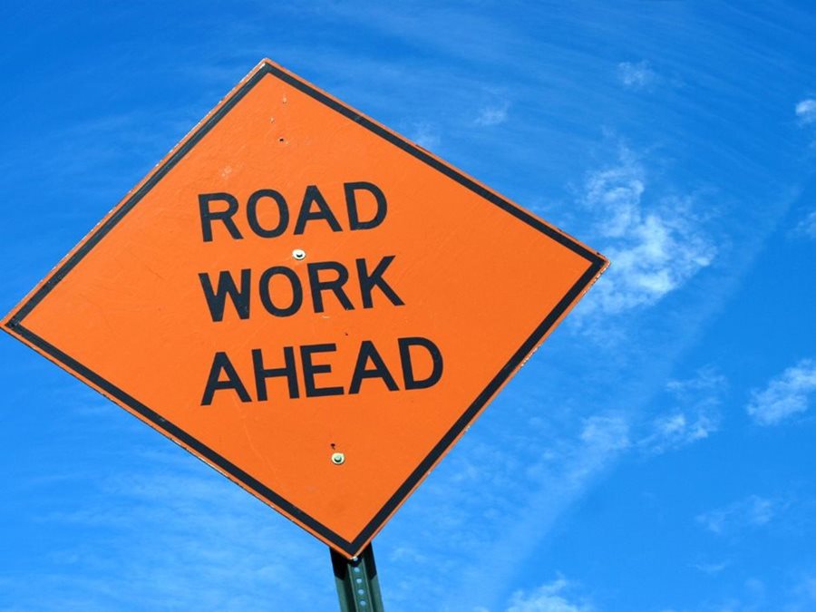 Orange sign that reads road work against blue sky background