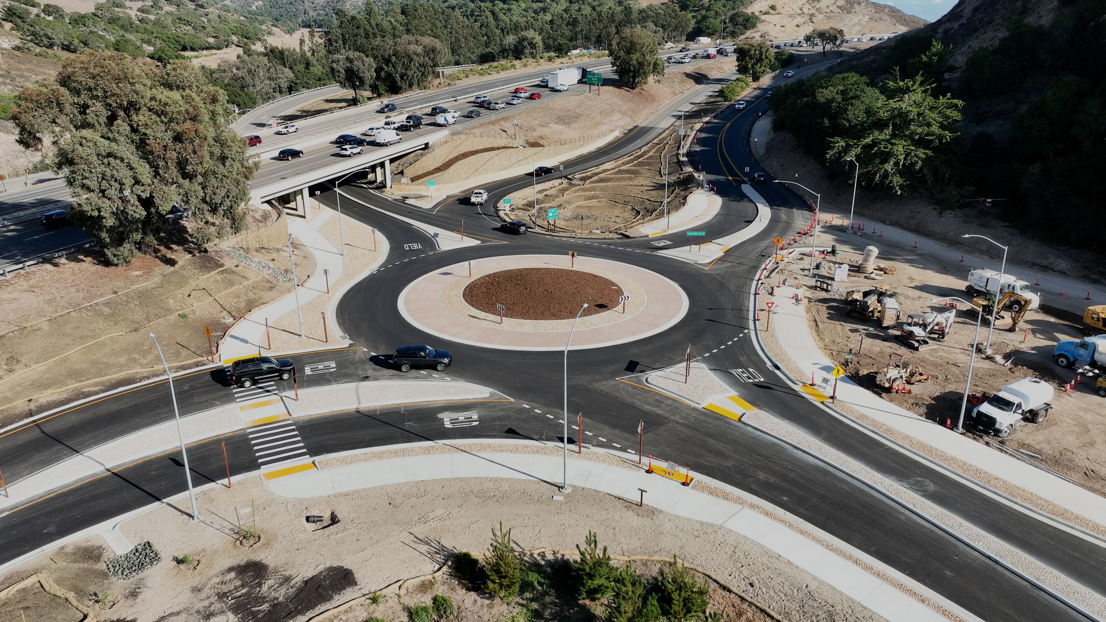 Aerial view of a roundabout with cars driving through and construction equipment on the roadside.