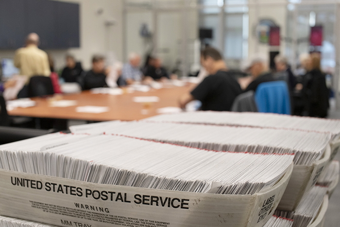 Vote by mail ballots in the foreground with election workers in the background