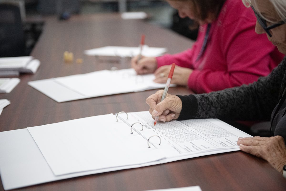 hands holding a red pen and making marks on a paper tally sheet