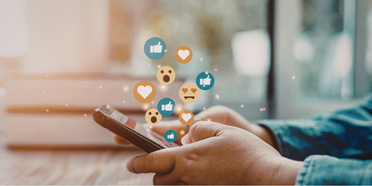 A person's hands holding a smartphone with social media reaction icons like hearts and thumbs-up floating above it.