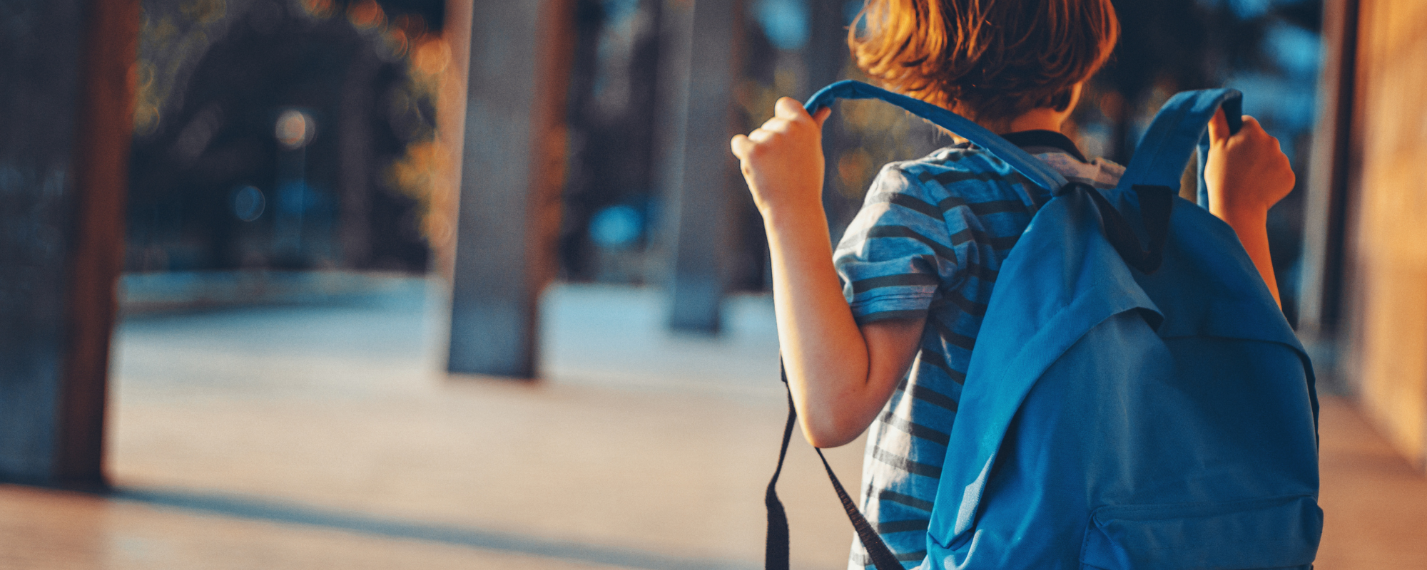 Young boy putting on his blue backpack