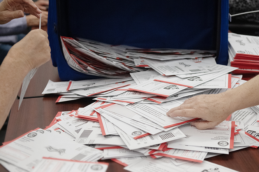 hands sorting through a pile of mail ballot return envelopes on a table
