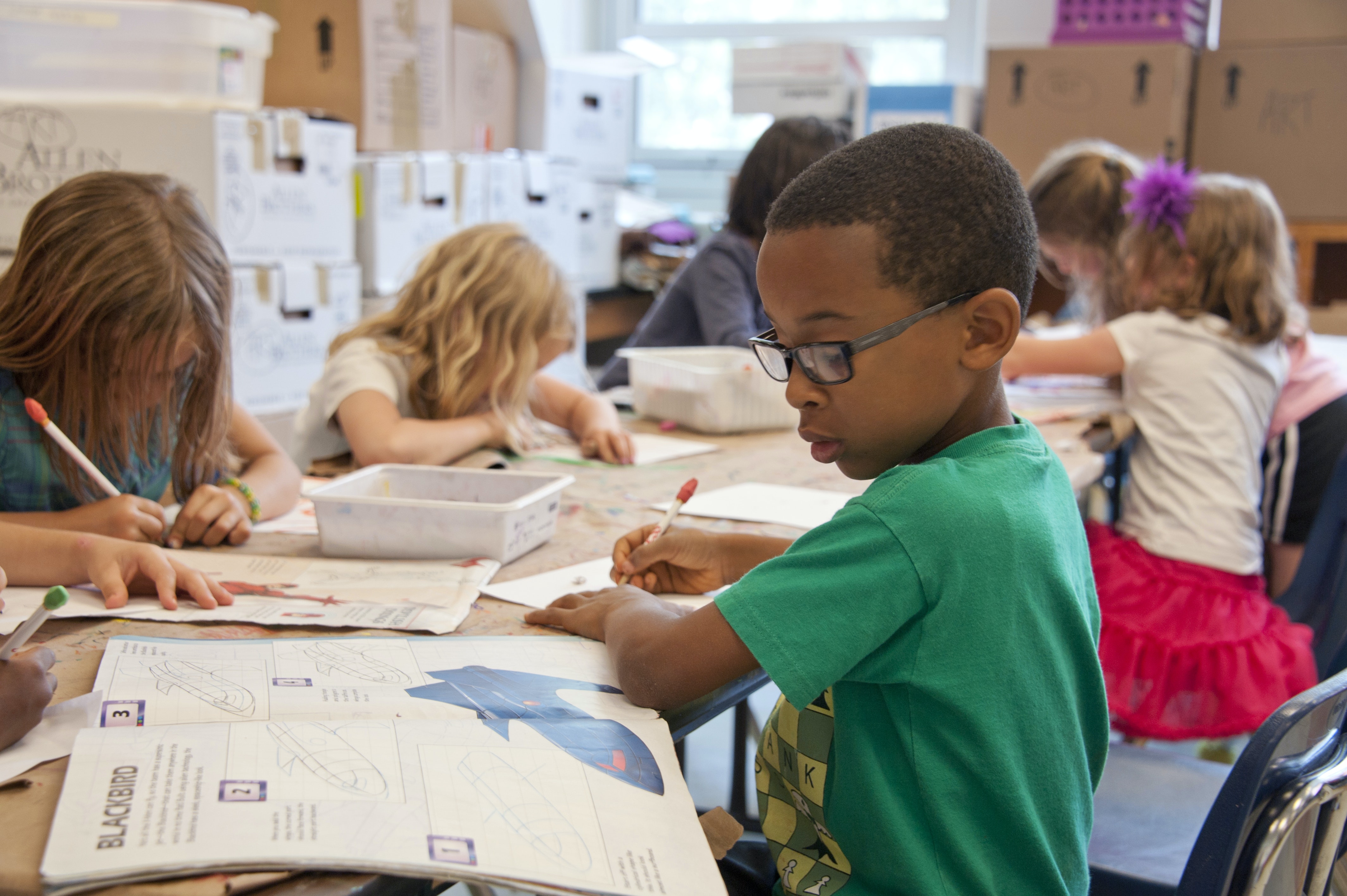 Multiple children sitting around a table working on school work.