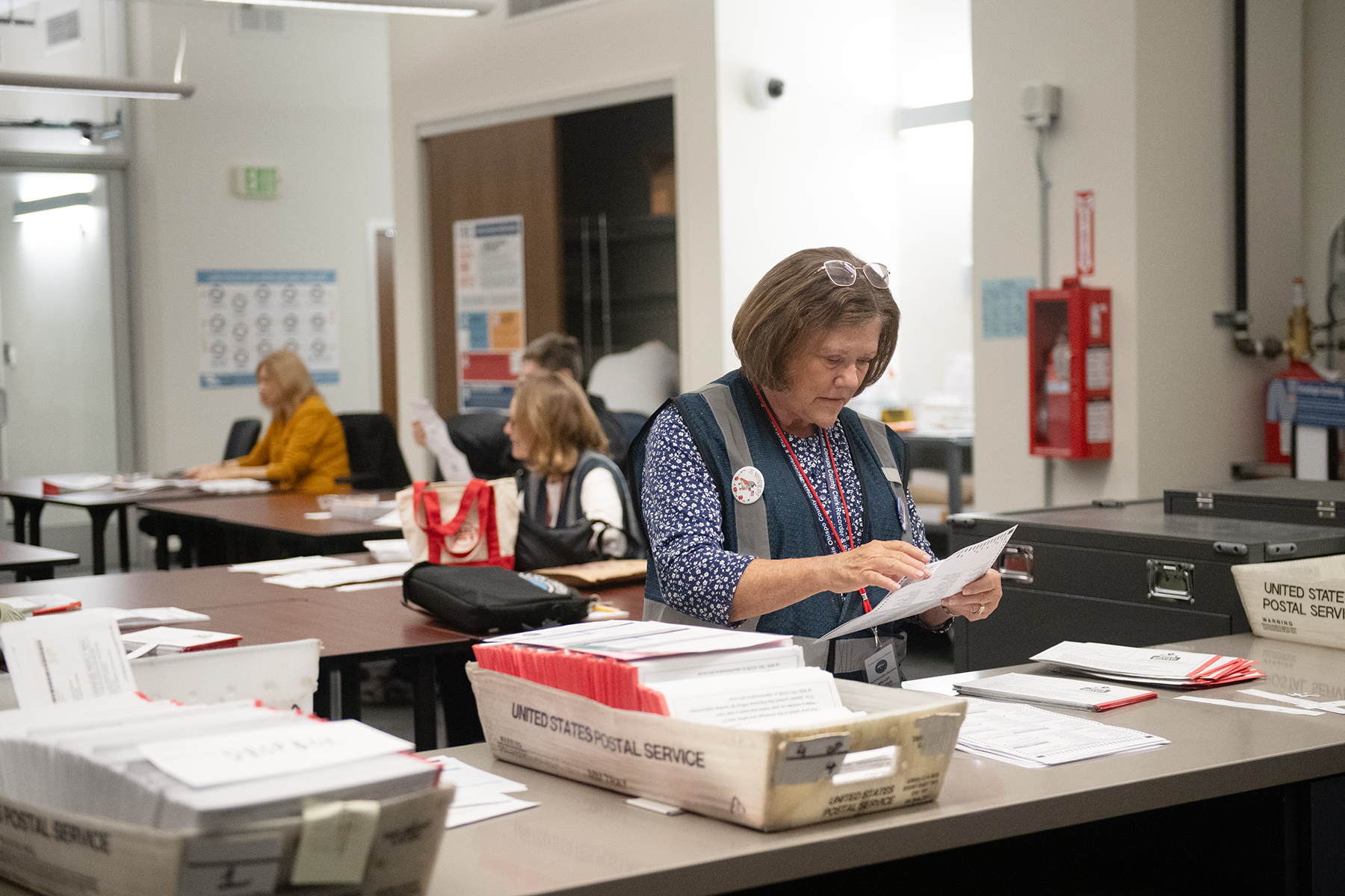 A woman standing at a counter sorting mail ballots