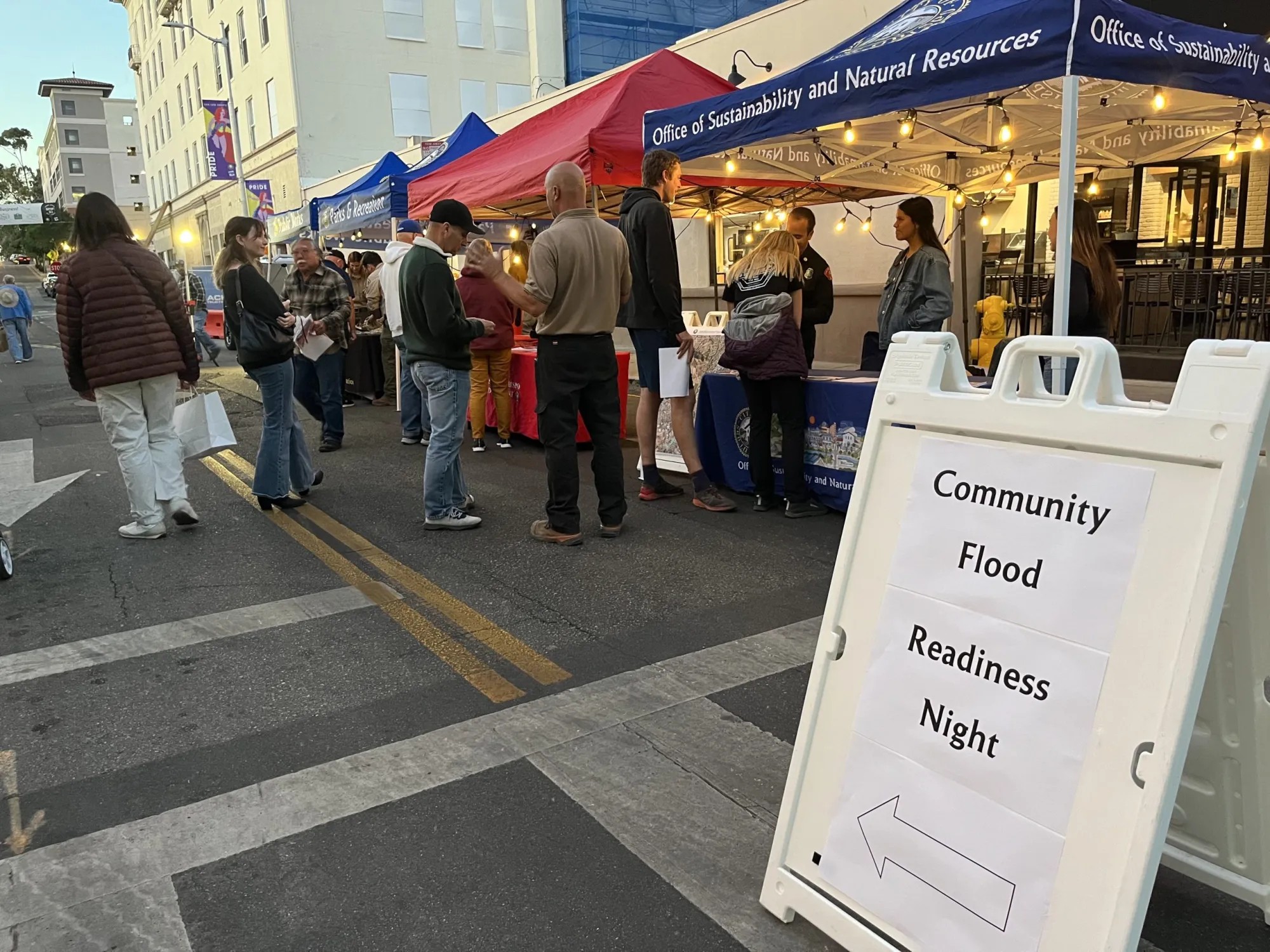 People gather at outdoor information booths, with a sign in front reading “Community Flood Readiness Night"