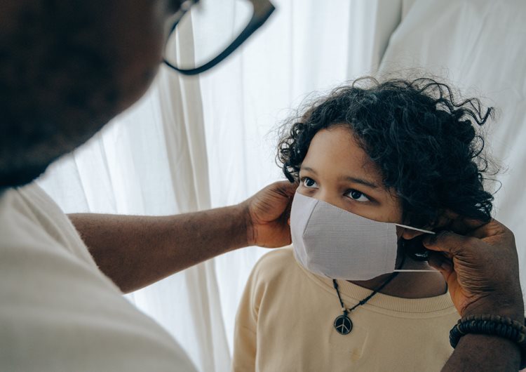 Man putting a medical mask on the face of a child.