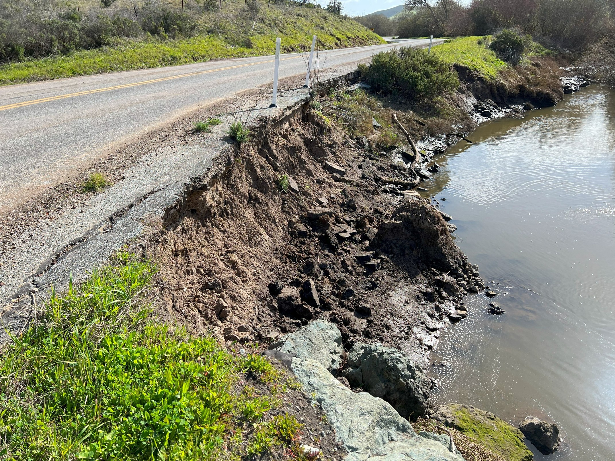 A portion of exposed soil between Turri Road and the creek below, trees in the background