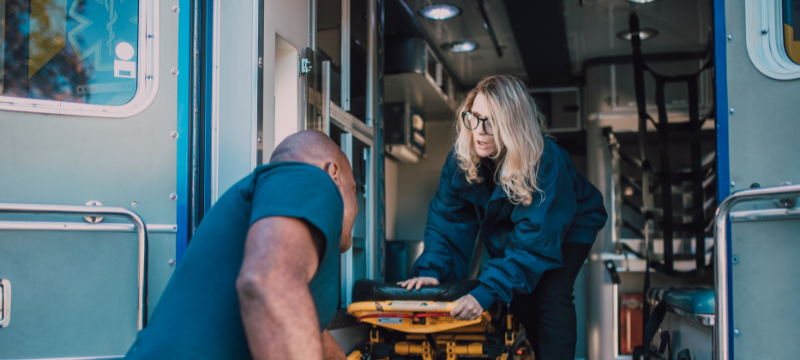 Emergency medical care represented by a woman and man rolling a stretcher into an ambulance.