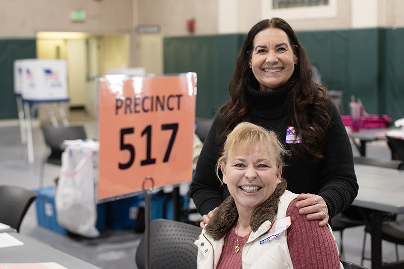 Two smiling women pose near a precinct sign