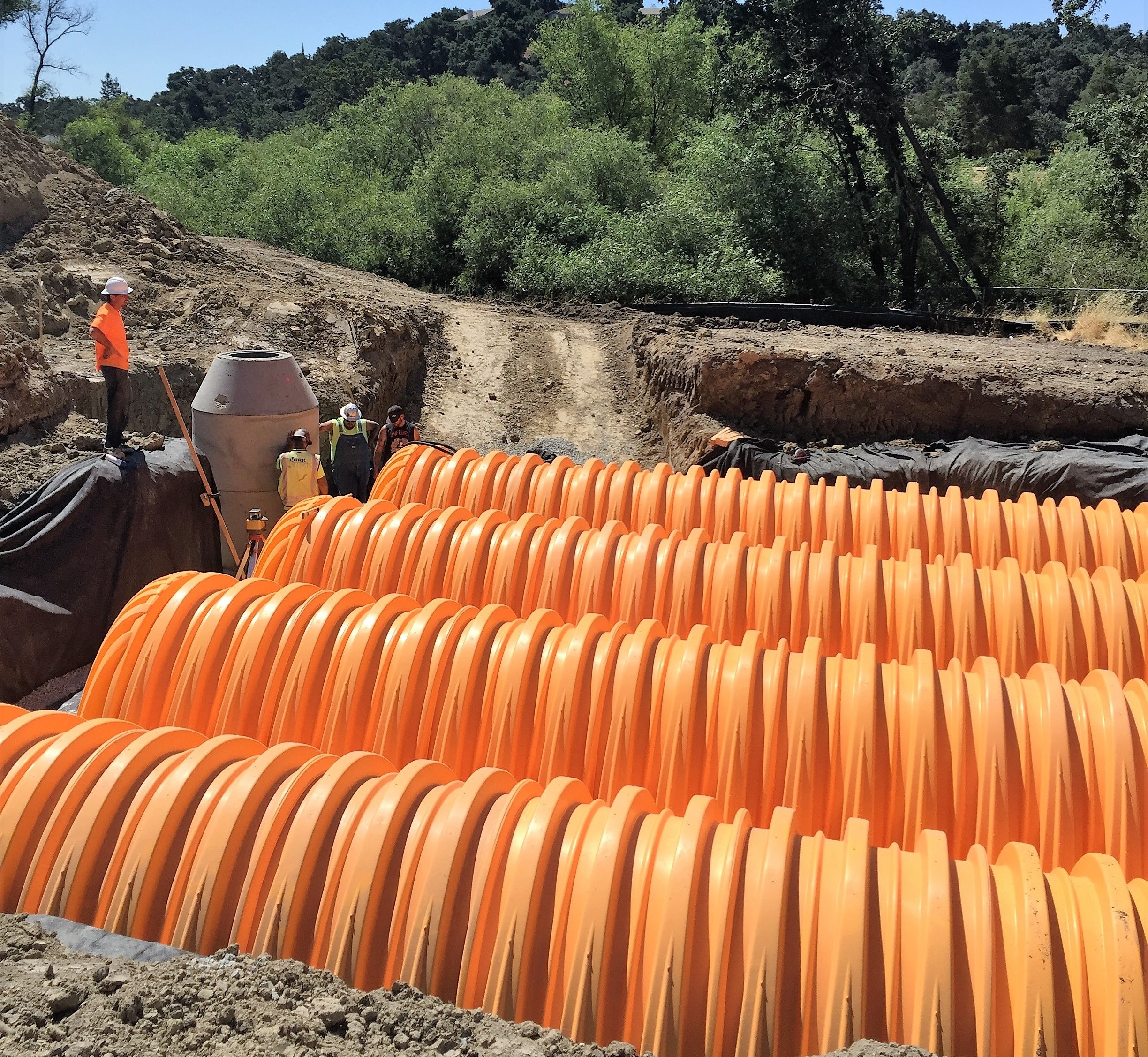 Construction workers in high-vis vests oversee large orange filtration system installation