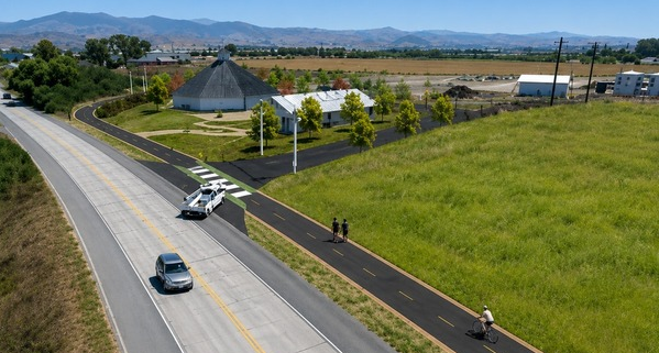 Aerial view of a paved bike and pedestrian path alongside a rural road and grassy fields.