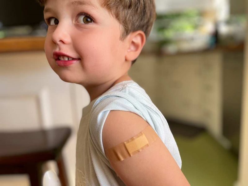 Young boy in a yellow t-shirt with a bandaid on his shoulder from vaccination.