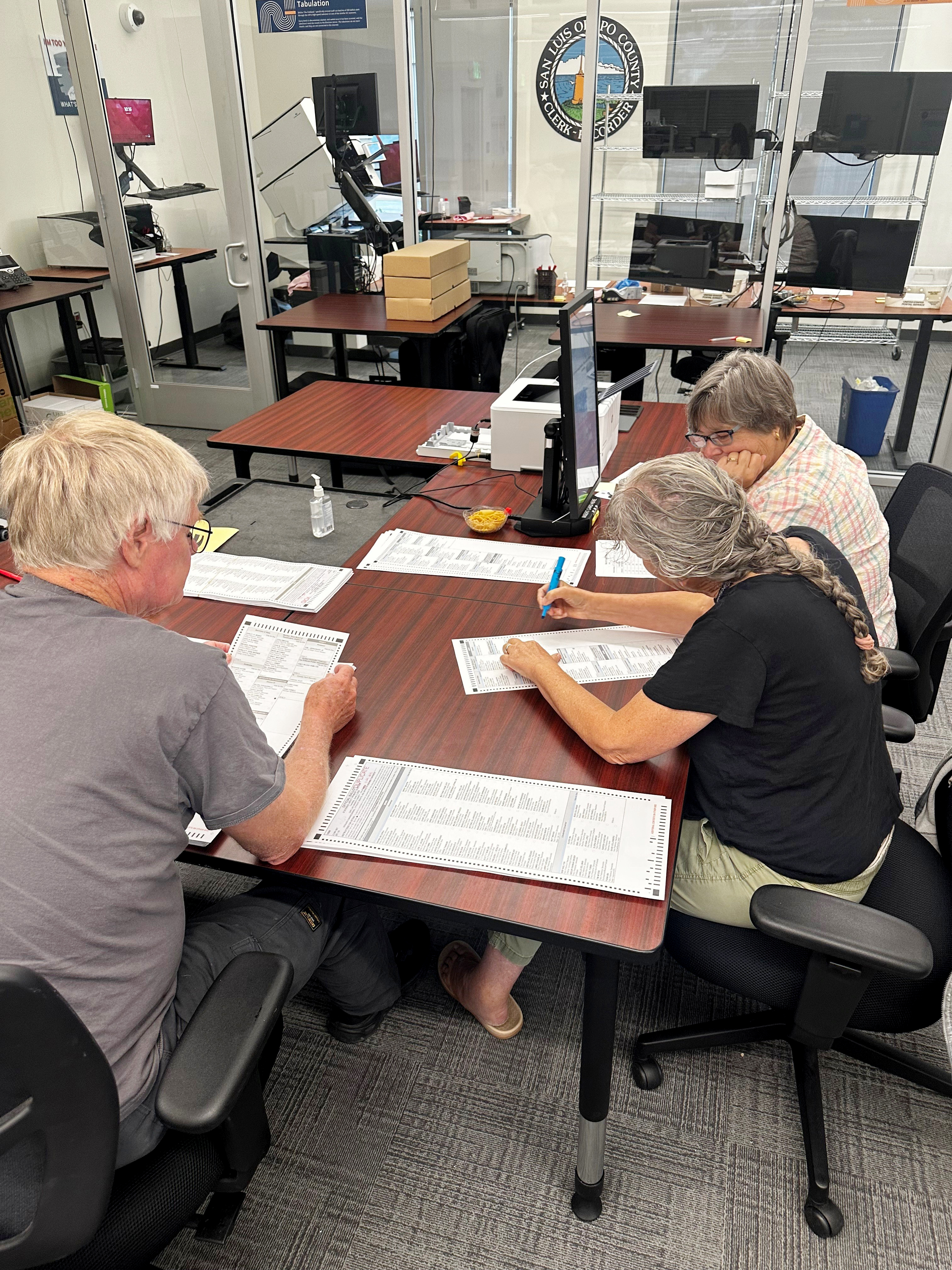 Three people sit at a table analyzing ballots
