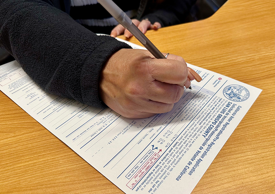 A woman's hand holding a pen over a San Luis Obispo County voter registration card